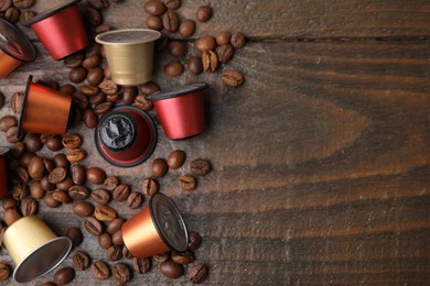 Many coffee capsules and beans on wooden table, flat lay. Space for text