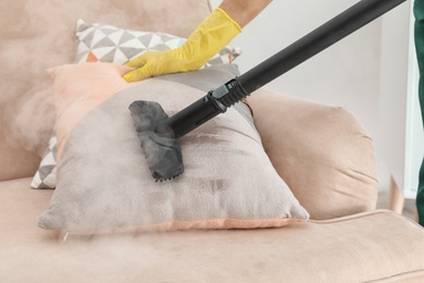 Janitor removing dirt from sofa cushion with steam cleaner, closeup