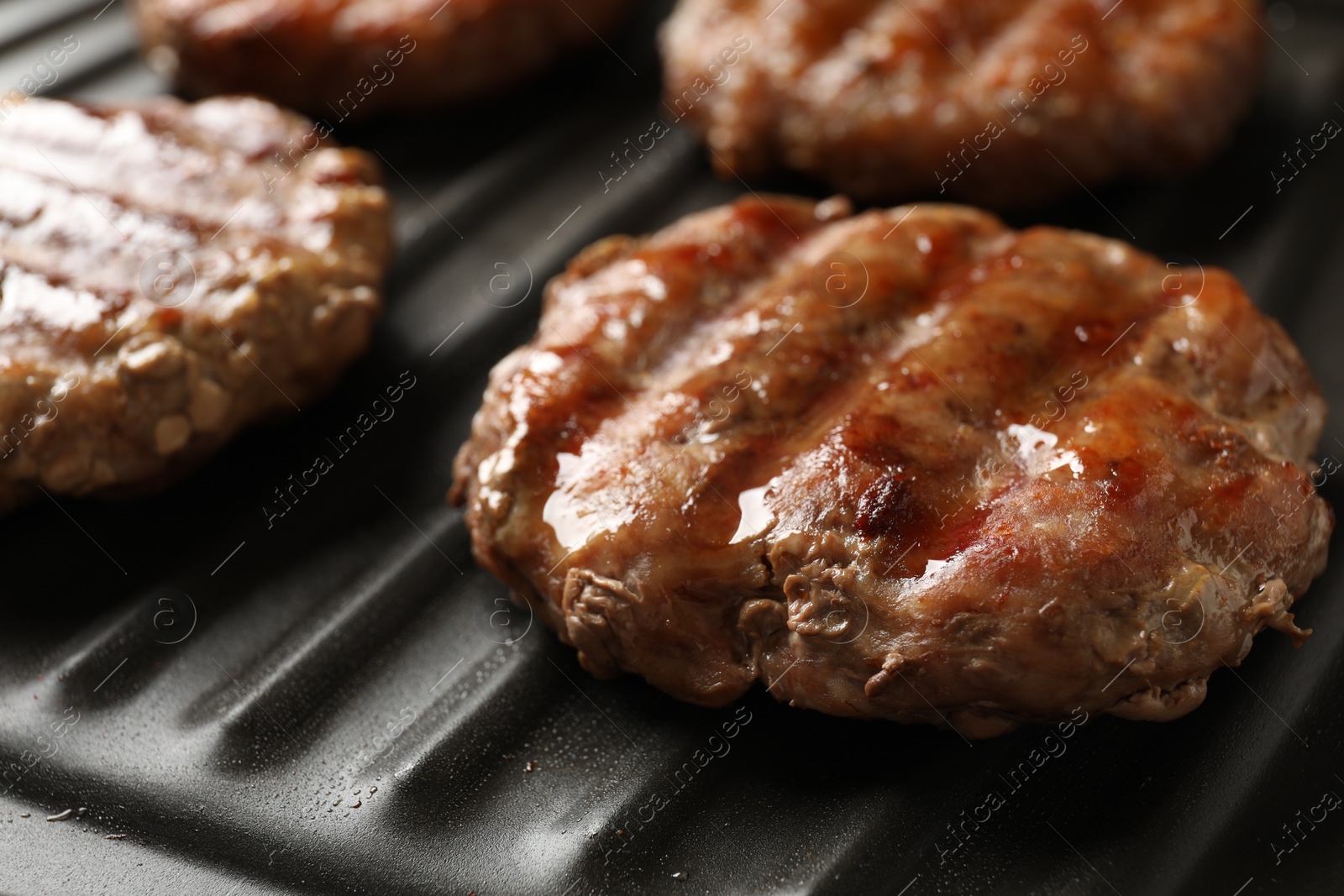 Photo of Delicious hamburger patties cooking on electric grill, closeup