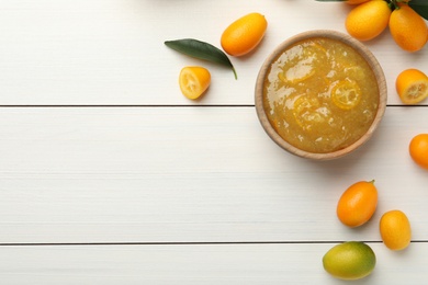 Photo of Delicious kumquat jam in bowl and fresh fruits on white wooden table, flat lay. Space for text