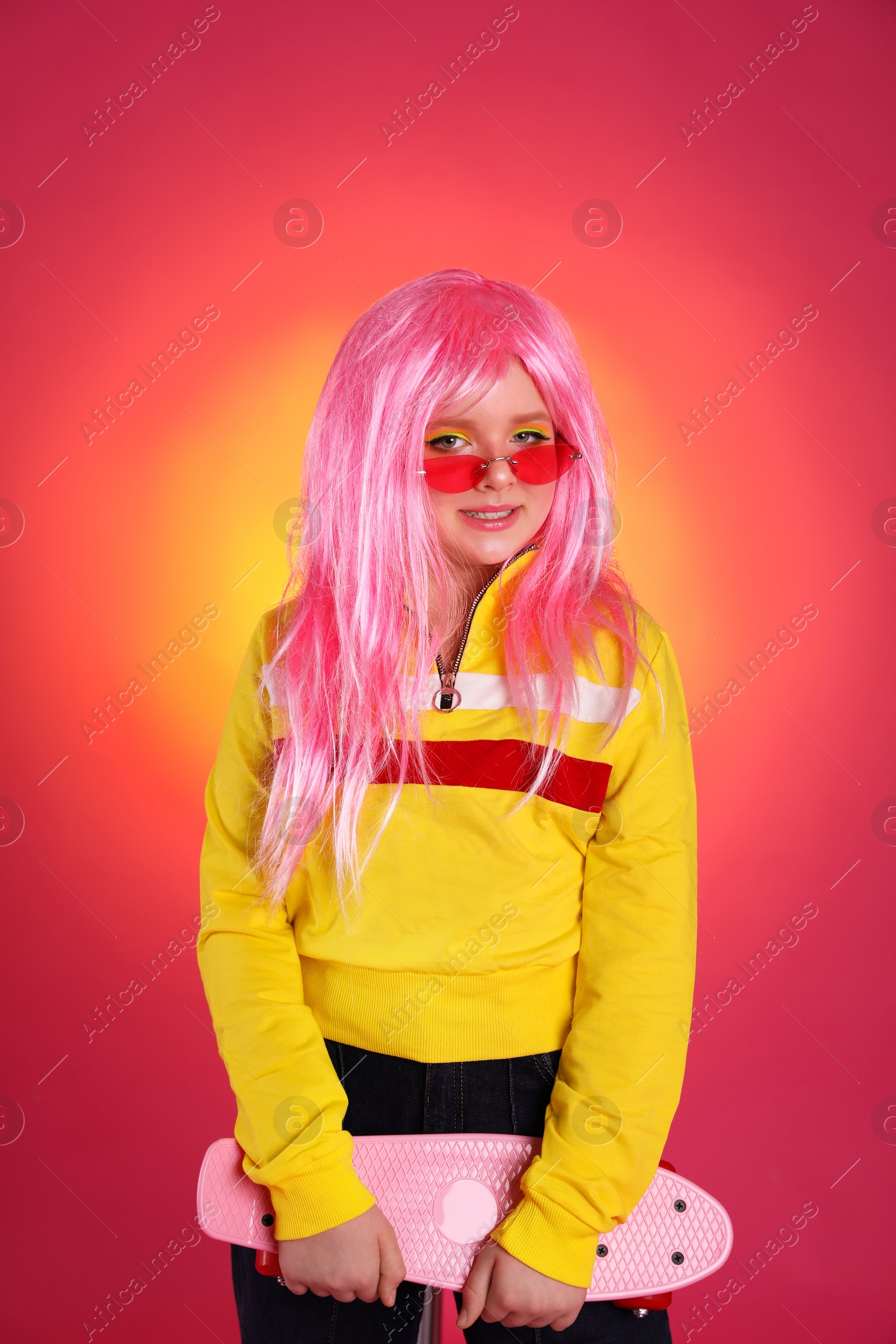 Photo of Cute indie girl with sunglasses and penny board on bright pink background