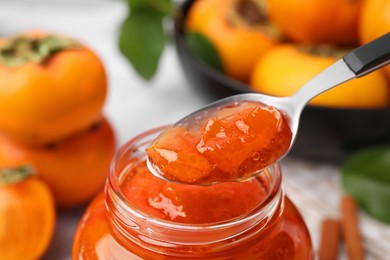 Jar and spoon of tasty persimmon jam, closeup