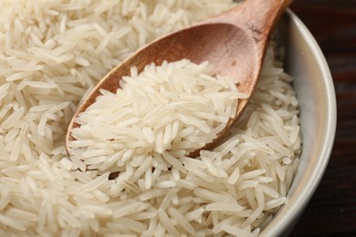 Photo of Raw basmati rice and wooden spoon in bowl on table, closeup