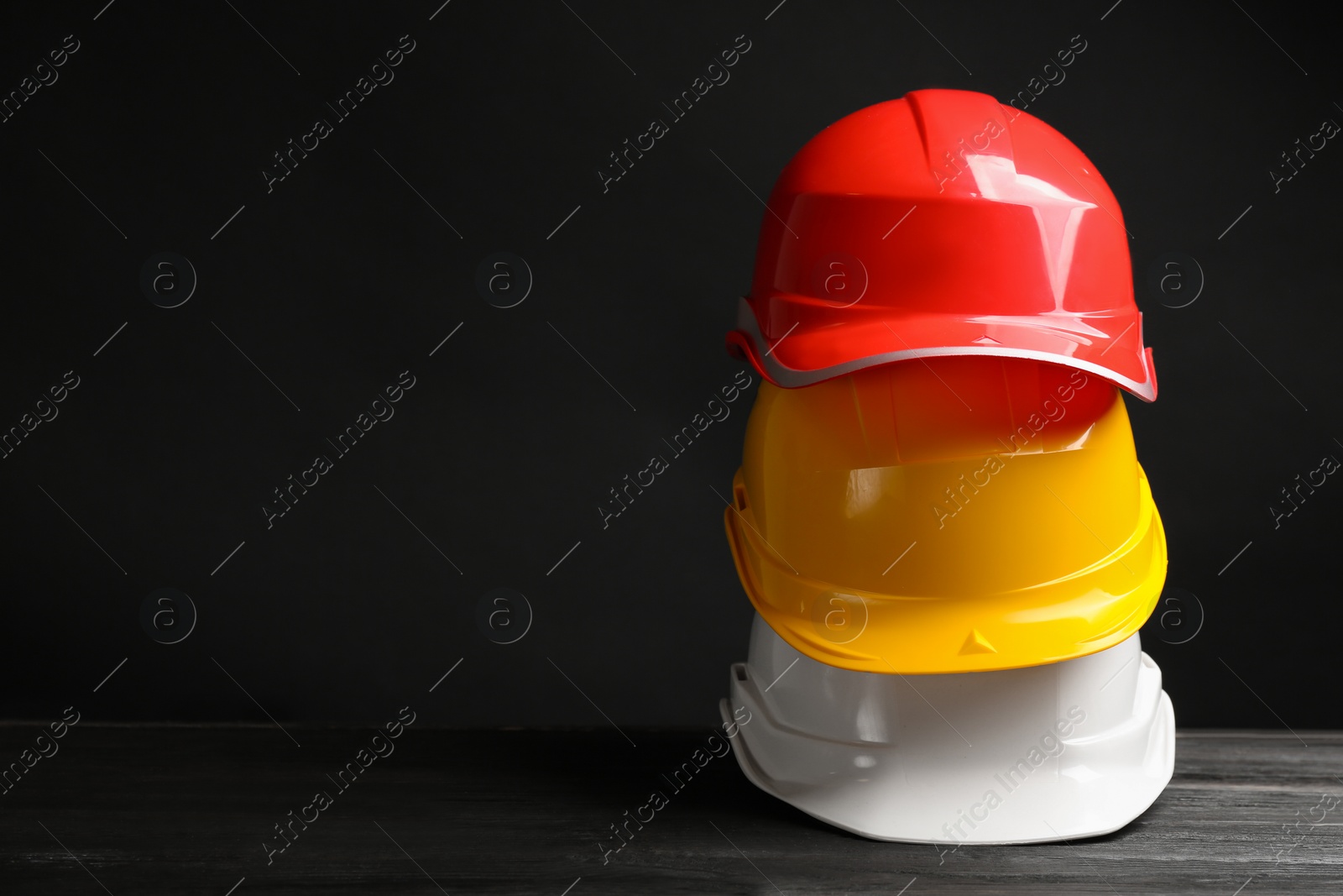 Photo of Stack of hard hats and space for text on black background. Safety equipment