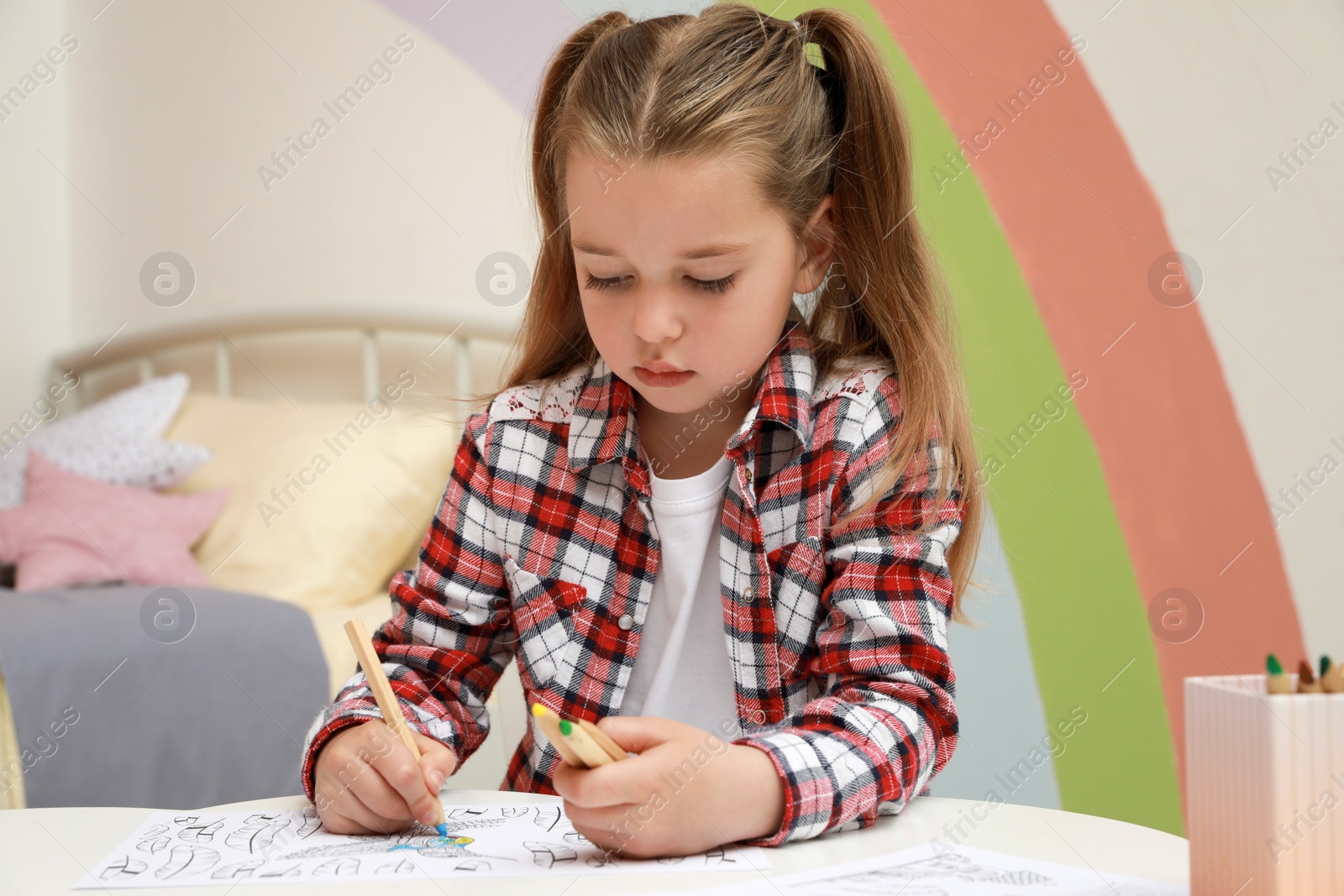 Photo of Little girl coloring antistress page at table indoors