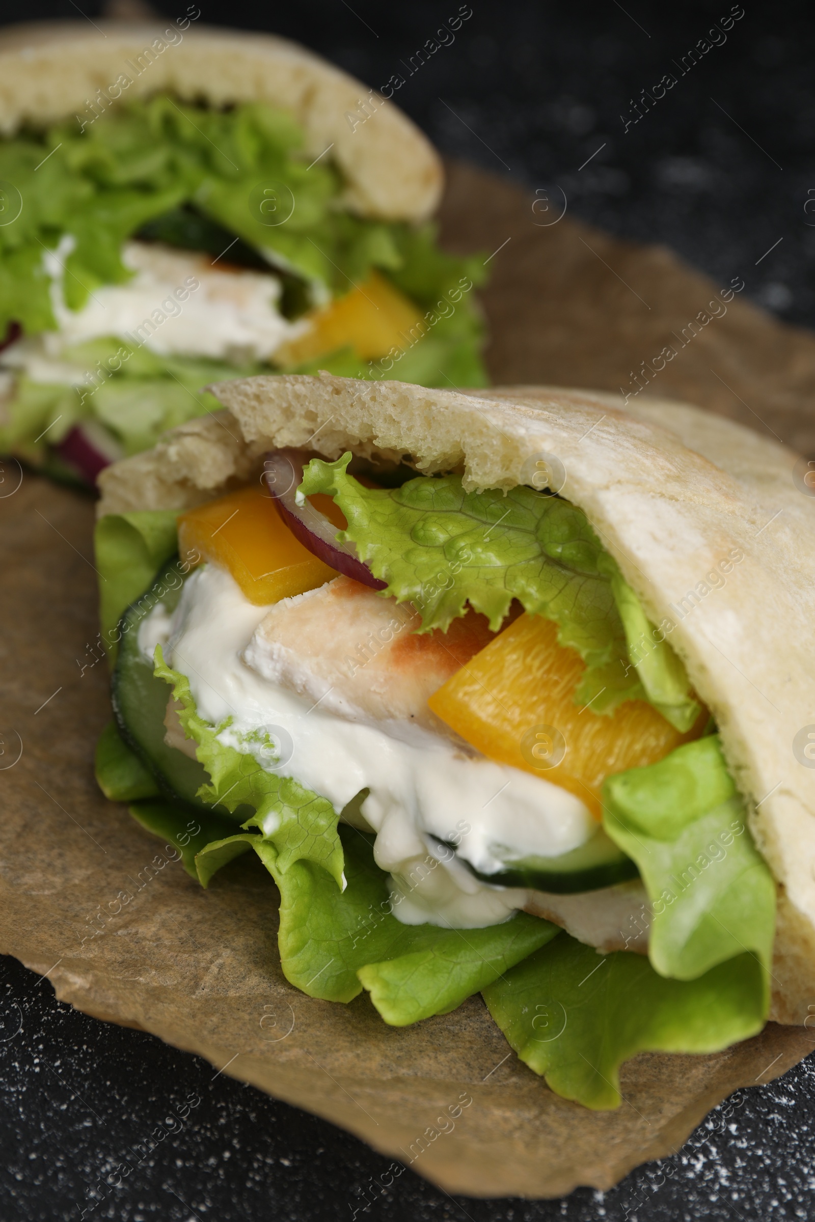 Photo of Delicious pita sandwiches with chicken breast and vegetables on parchment paper, closeup