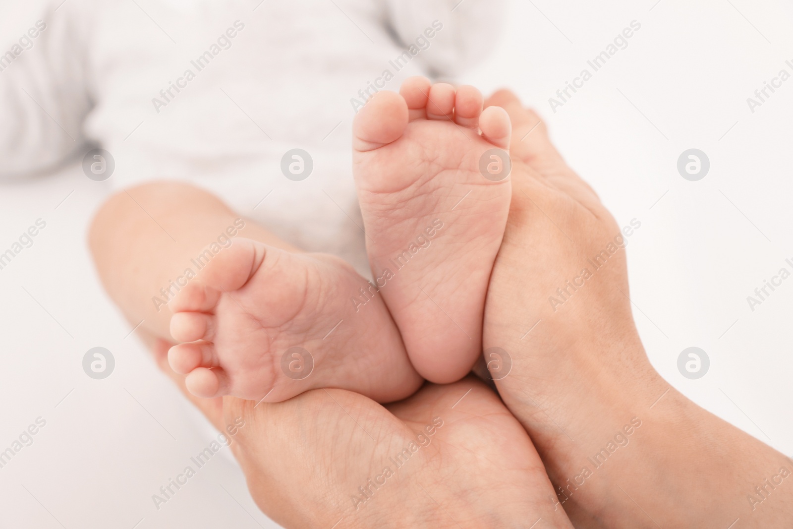 Photo of Mother holding baby's feet on light background, closeup