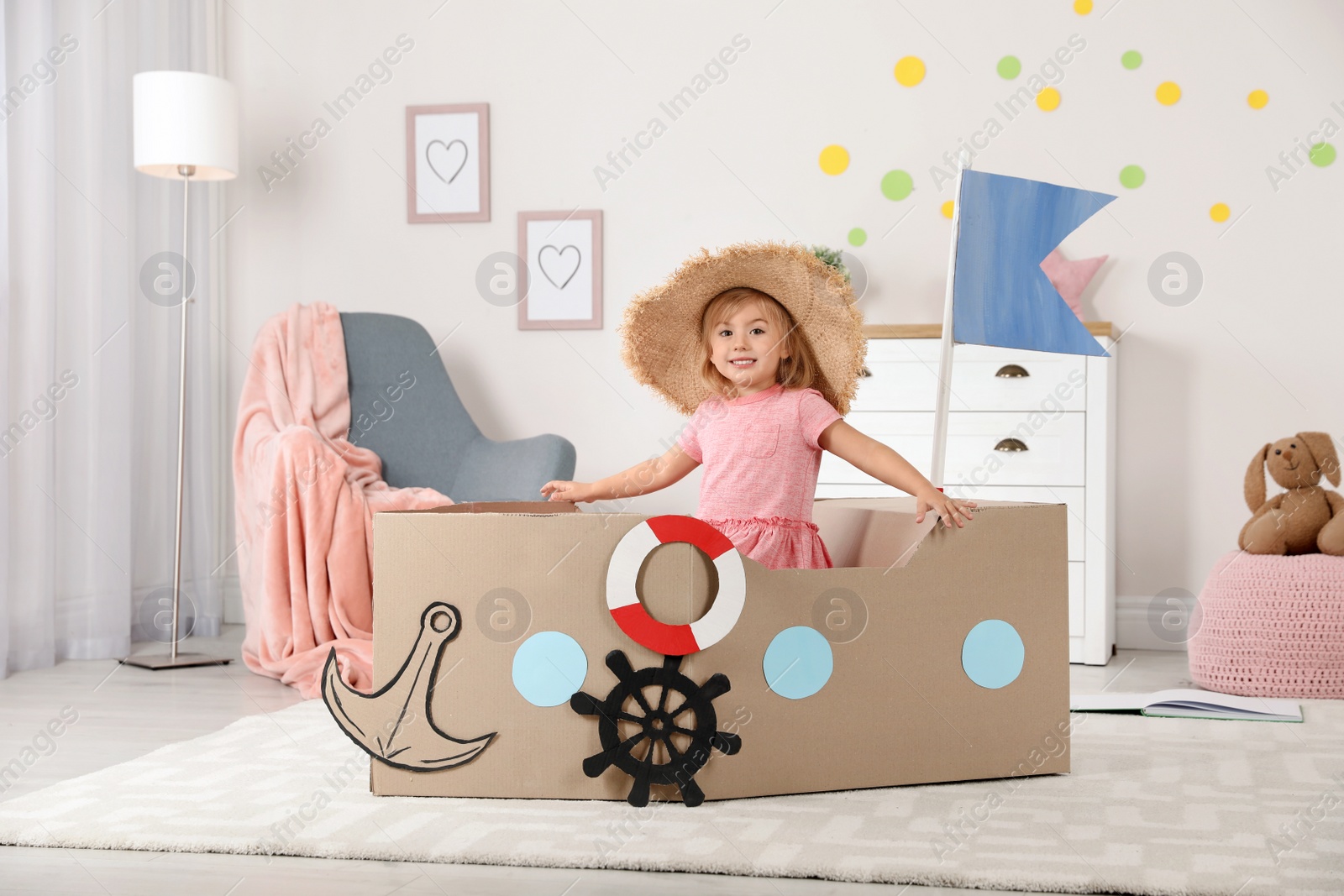 Photo of Cute little girl playing with cardboard ship at home