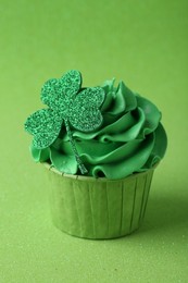 St. Patrick's day party. Tasty cupcake with clover leaf topper and cream on green background, closeup