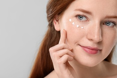 Beautiful woman with freckles and cream on her face against grey background, closeup. Space for text