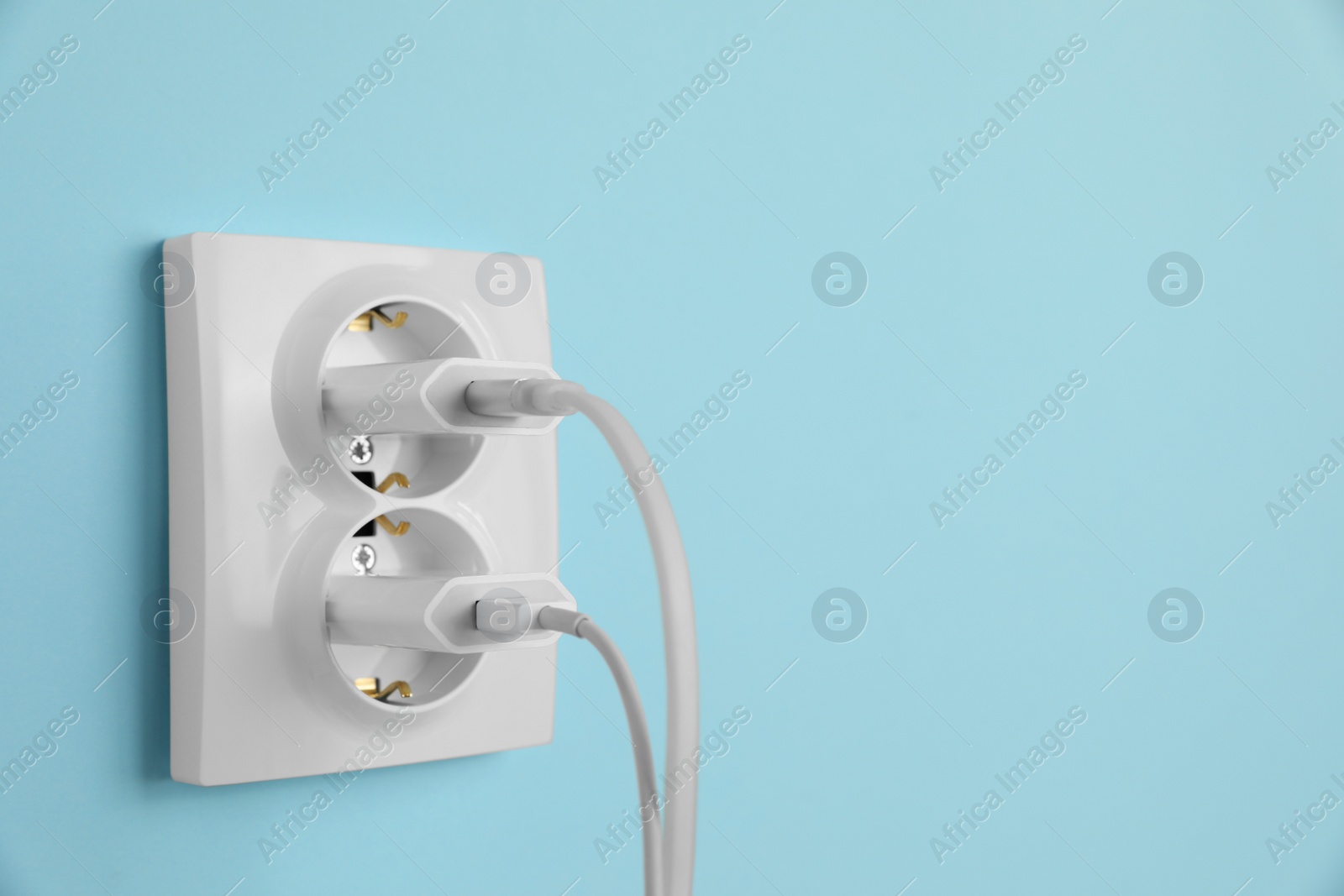 Photo of Charger adapters plugged into power sockets on light blue wall, space for text. Electrical supply