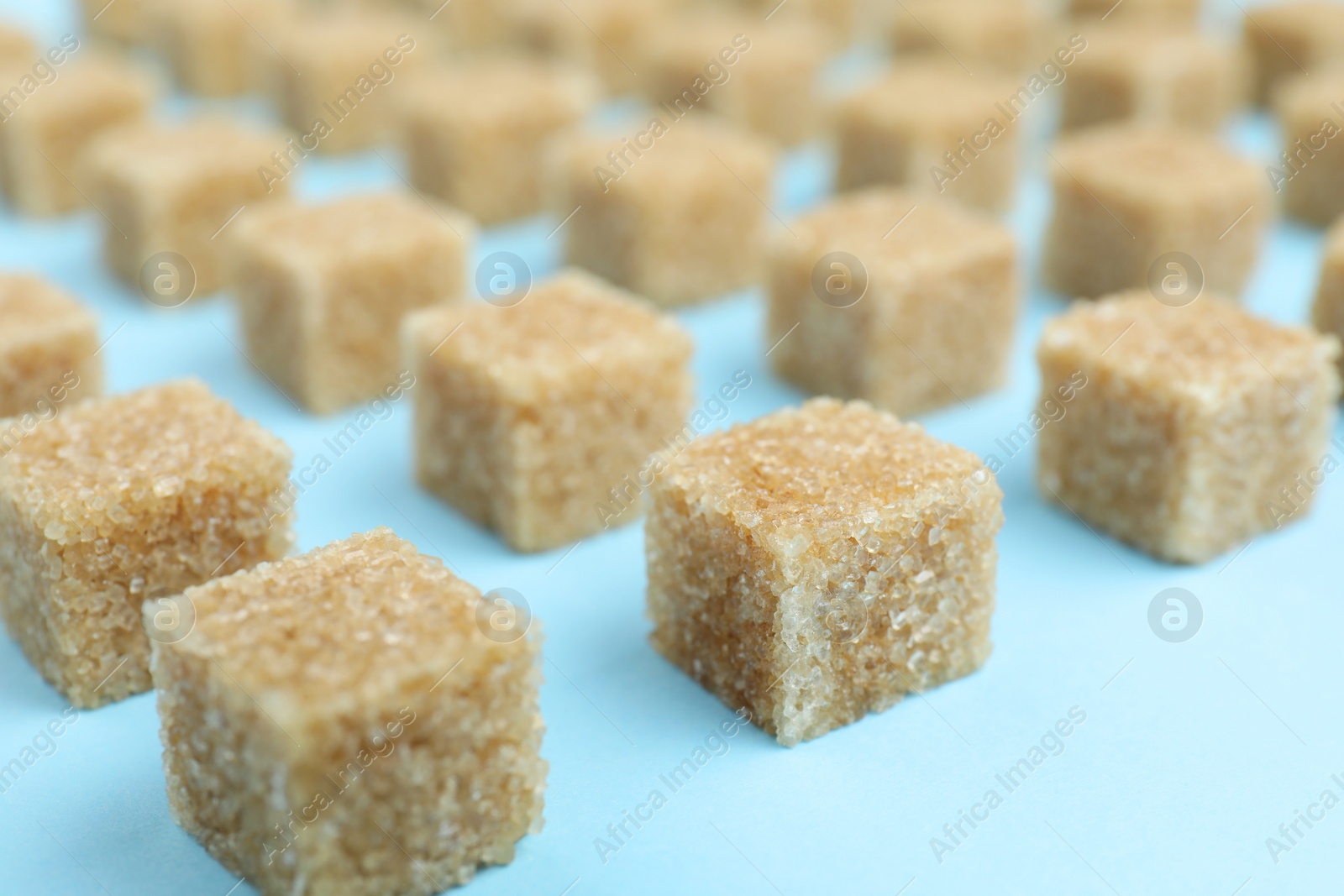 Photo of Brown sugar cubes on light blue background, closeup