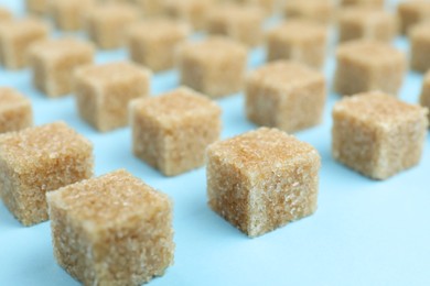 Photo of Brown sugar cubes on light blue background, closeup