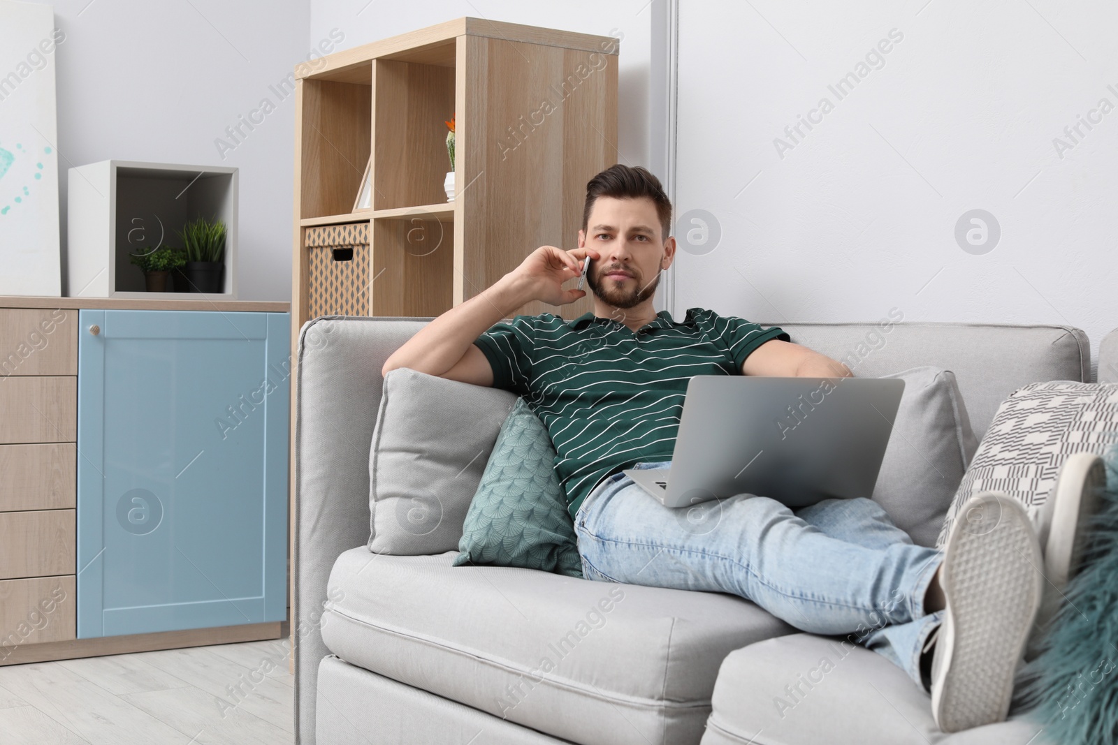 Photo of Young man working with laptop on sofa in home office