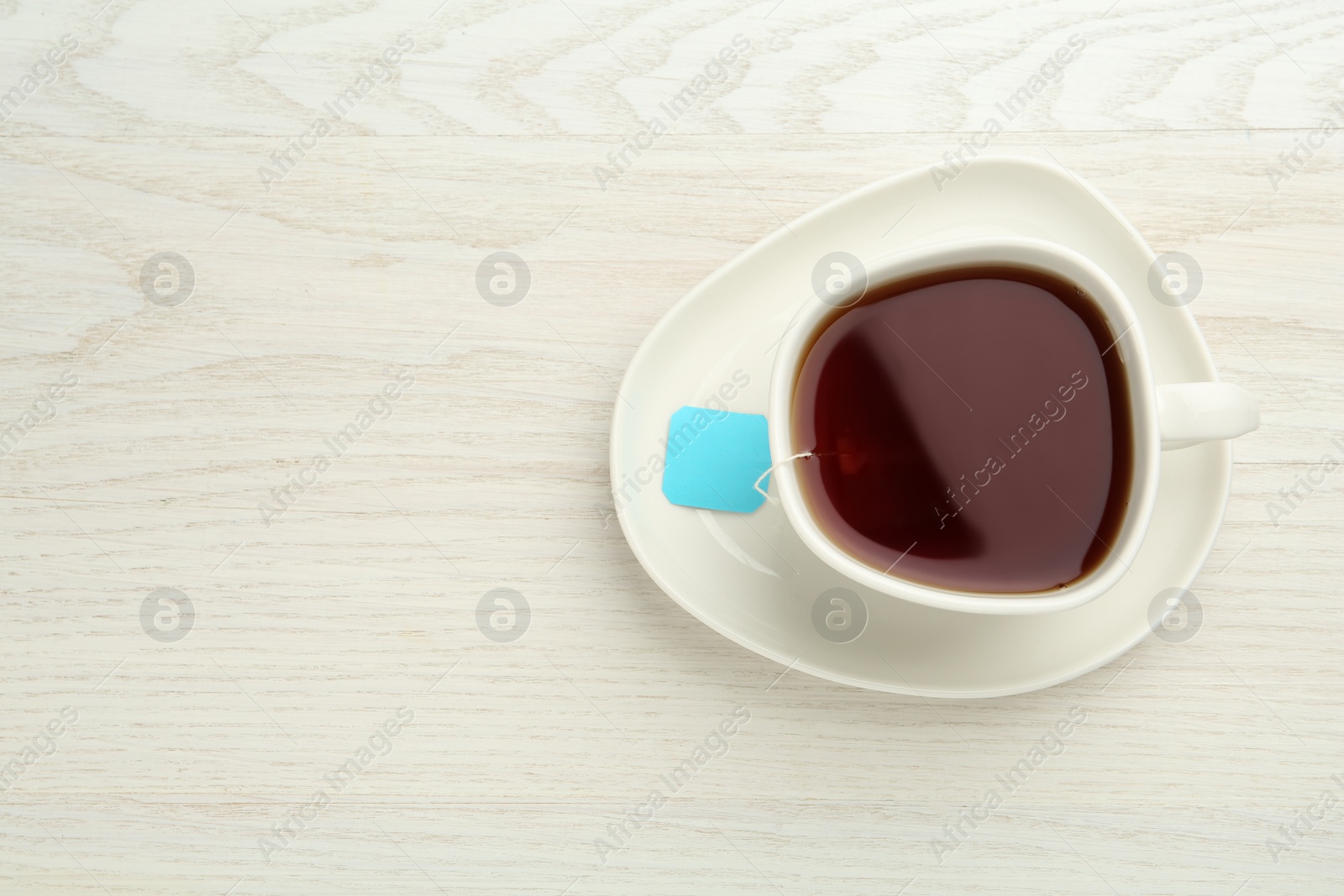 Photo of Tea bag in ceramic cup of hot water on white wooden table, top view. Space for text