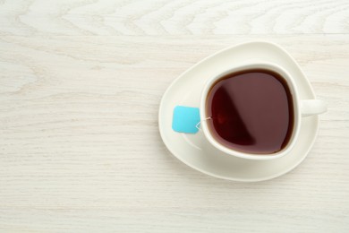 Photo of Tea bag in ceramic cup of hot water on white wooden table, top view. Space for text