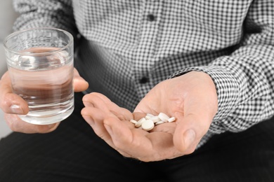 Photo of Senior man holding pills and glass of water, closeup