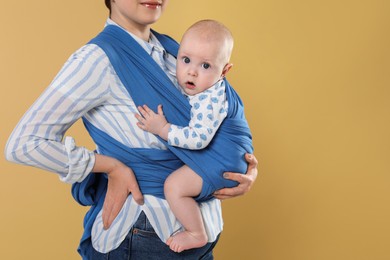 Photo of Mother holding her child in sling (baby carrier) on beige background, closeup. Space for text