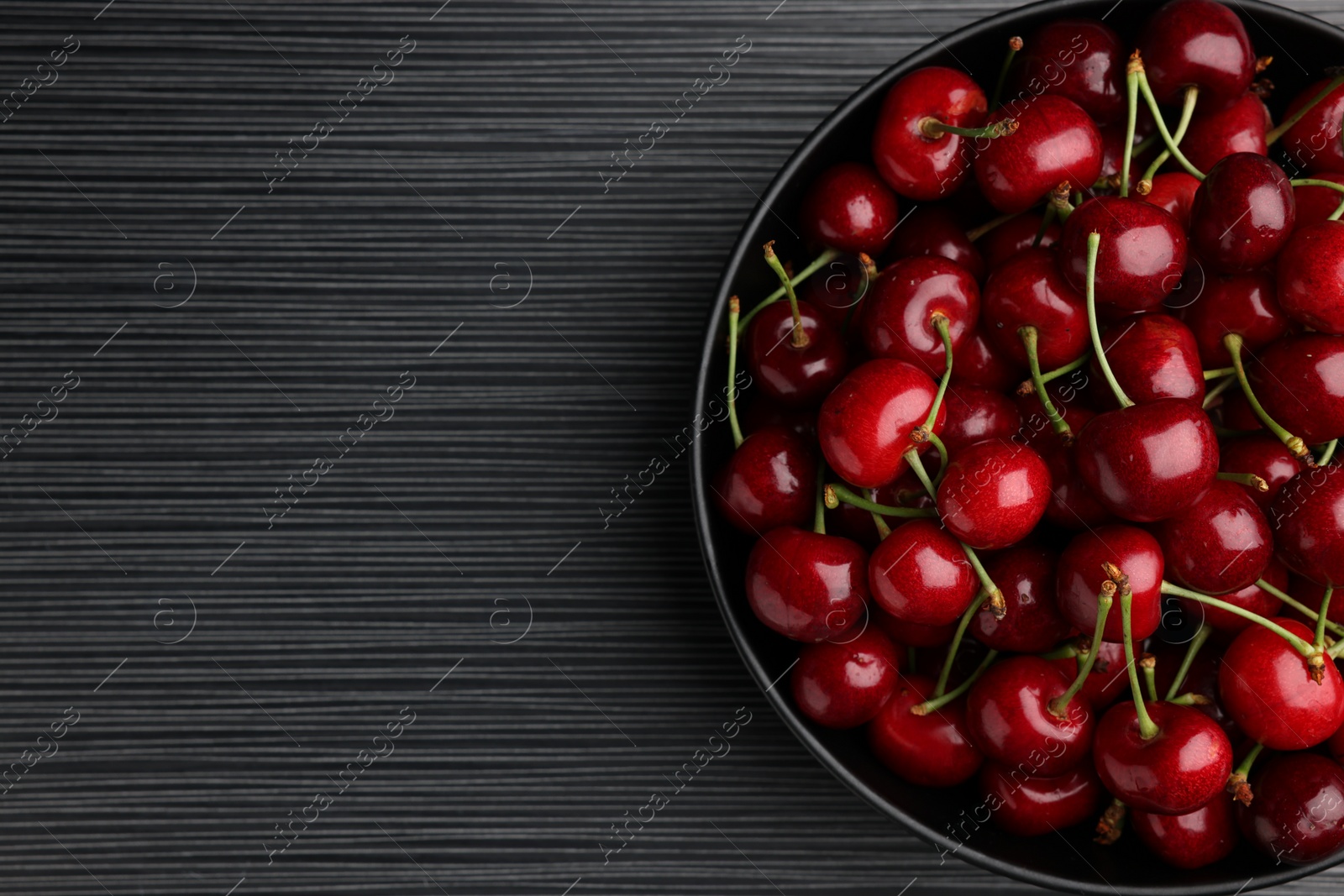 Photo of Bowl with ripe sweet cherries on dark wooden table, top view. Space for text