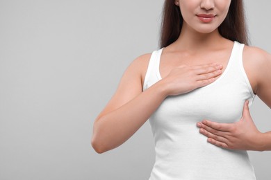 Woman doing breast self-examination on light grey background, closeup. Space for text