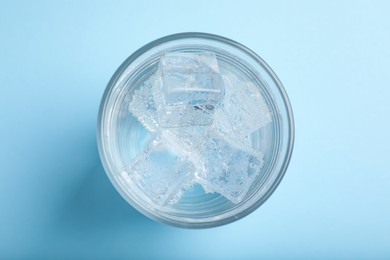 Photo of Glass of soda water with ice on light blue background, top view