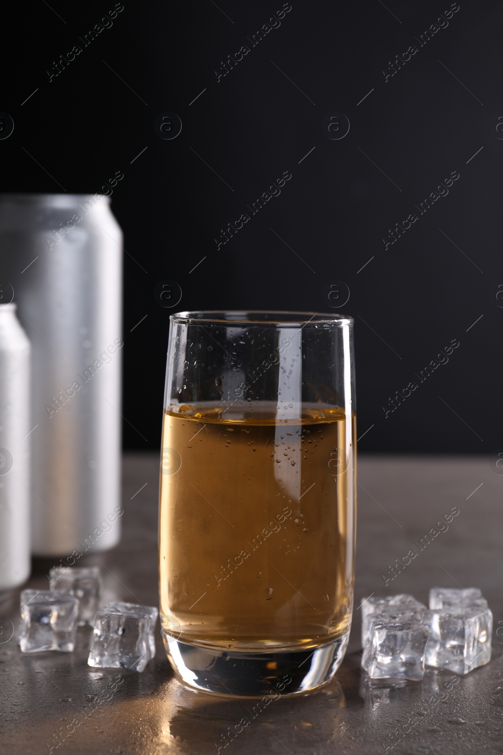 Photo of Energy drink in glass, aluminium cans and ice cubes on grey table