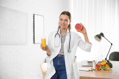 Nutritionist with glass of juice and grapefruit near desk in office