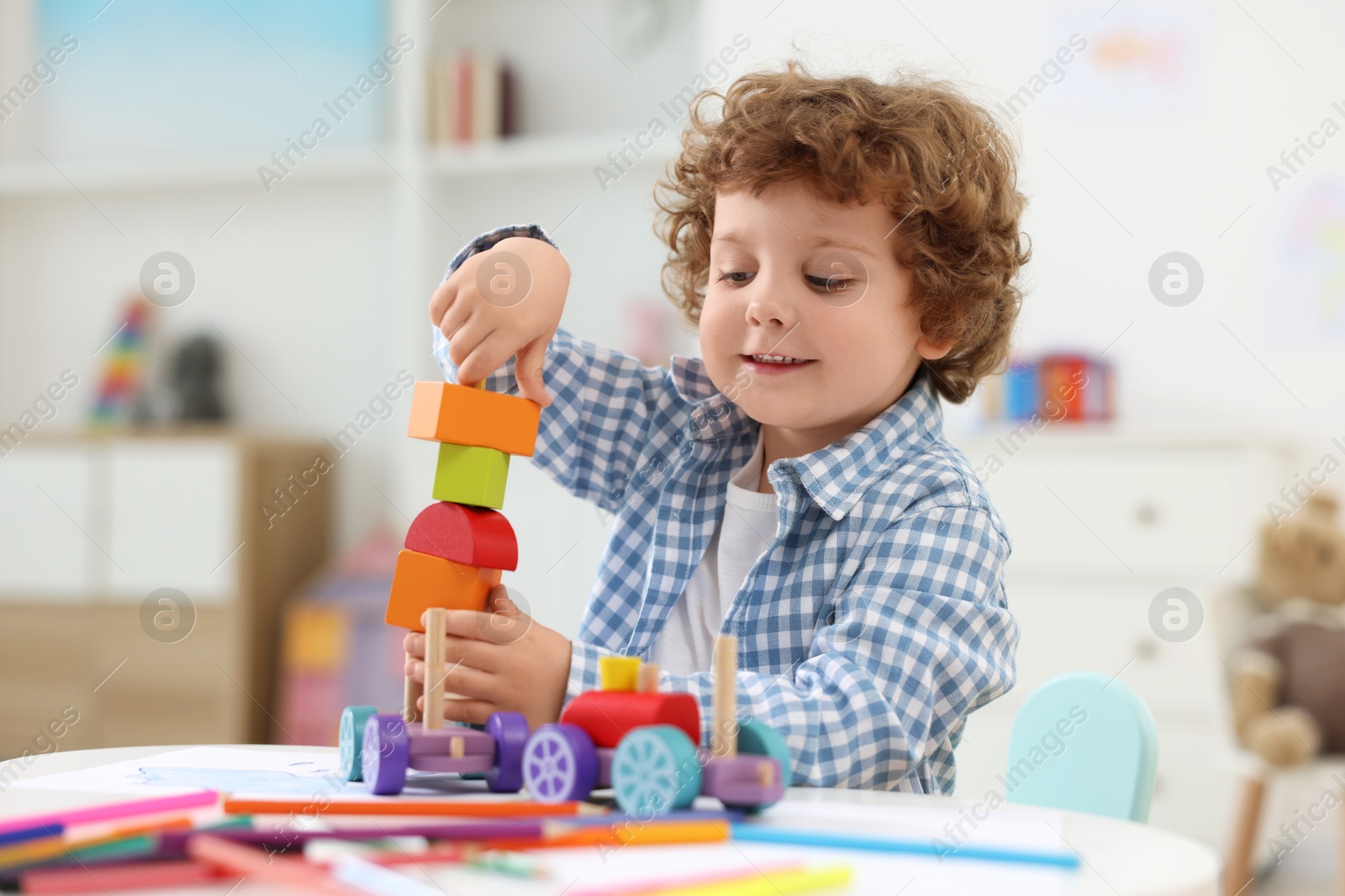 Photo of Cute little boy playing with wooden toys at white table in kindergarten