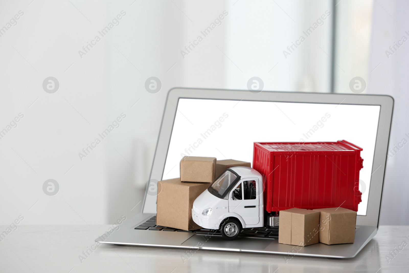 Photo of Laptop and truck model with boxes on table indoors. Courier service