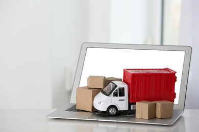 Laptop and truck model with boxes on table indoors. Courier service