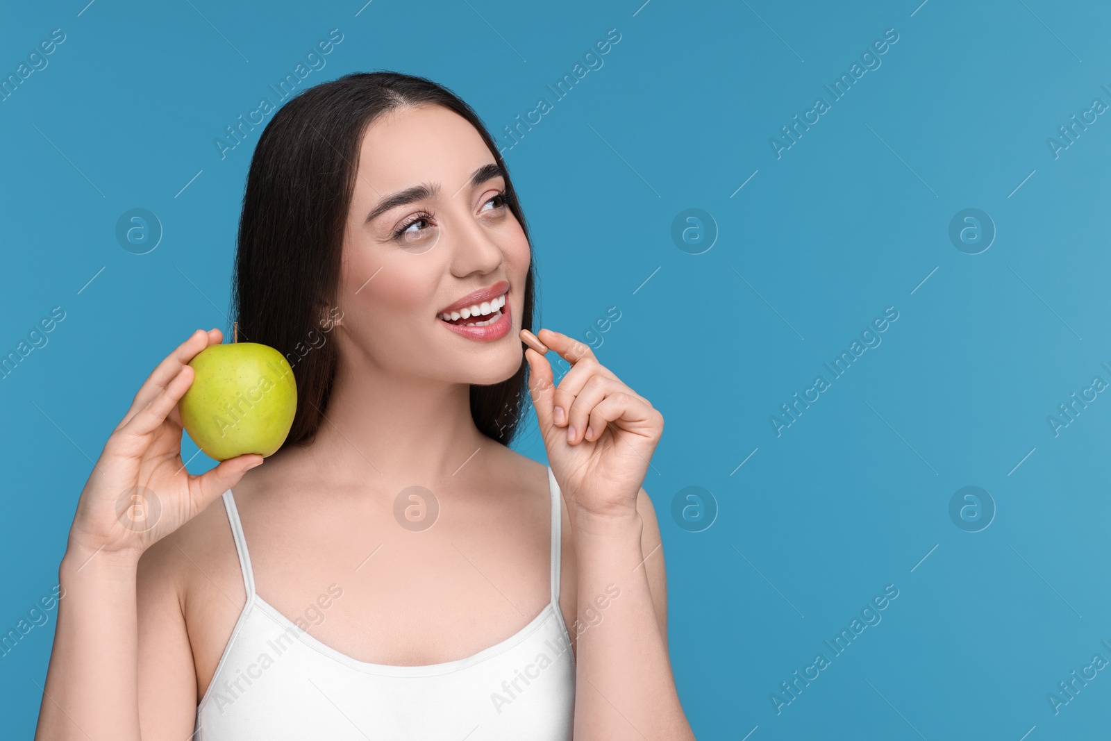 Photo of Beautiful young woman with vitamin pill and apple on light blue background. Space for text