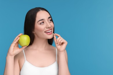 Beautiful young woman with vitamin pill and apple on light blue background. Space for text