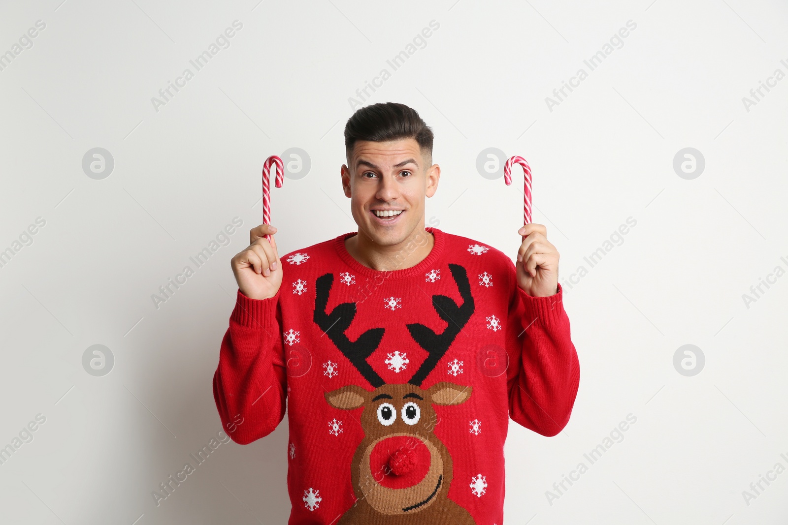 Photo of Happy man in Christmas sweater with candy canes on white background