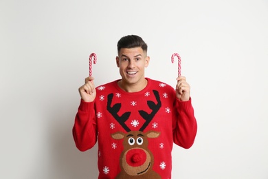 Photo of Happy man in Christmas sweater with candy canes on white background