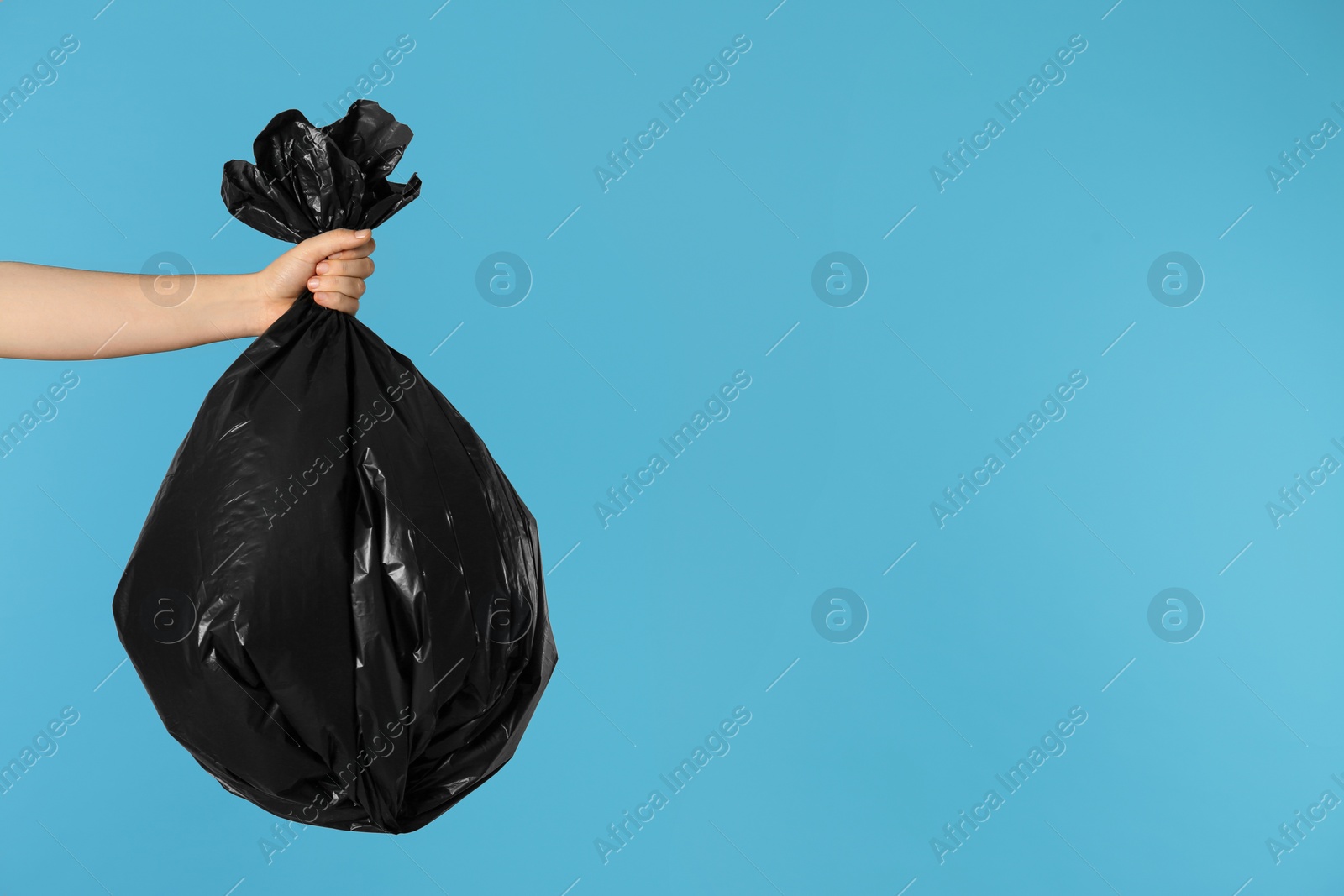 Photo of Woman holding trash bag full of garbage on light blue background, closeup. Space for text