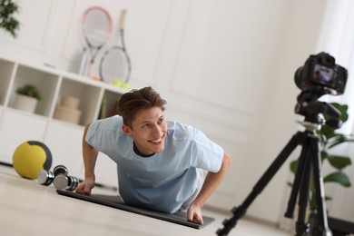 Smiling sports blogger doing push-ups while recording fitness lesson with camera at home