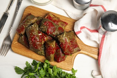Photo of Delicious stuffed grape leaves with tomato sauce on white wooden table, flat lay