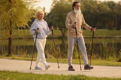 Photo of Senior man and woman performing Nordic walking outdoors