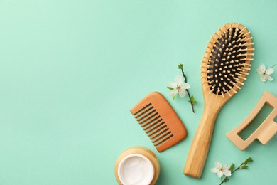 Flat lay composition with wooden hairbrush and flower branches on turquoise background. Space for text
