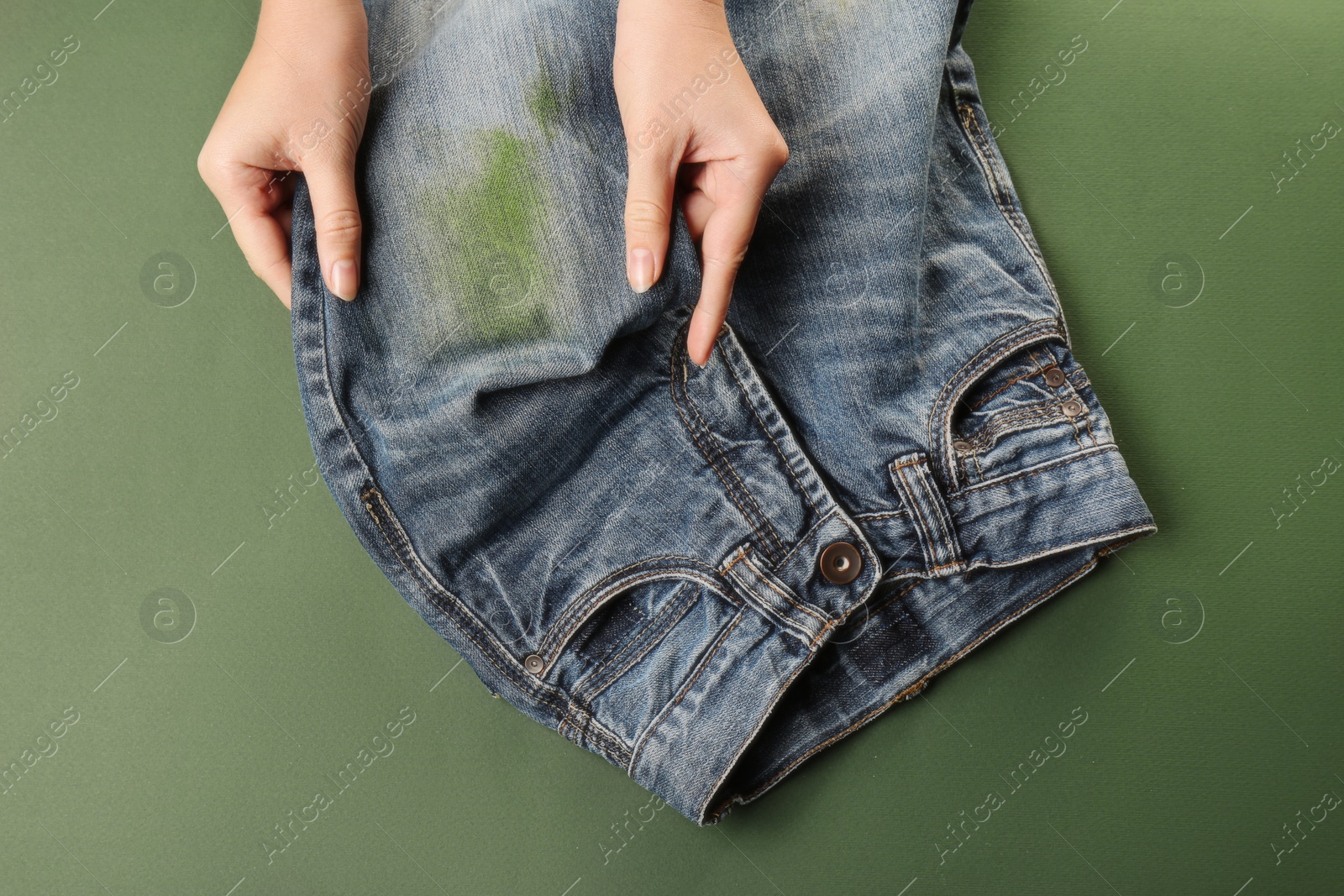 Photo of Woman holding jeans with stain on green background, top view