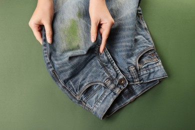 Woman holding jeans with stain on green background, top view