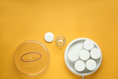 Modern yogurt maker with jars on orange background, flat lay. Space for text