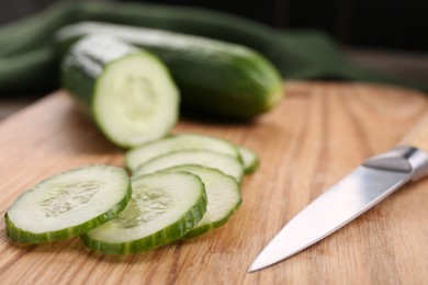 Photo of Cut cucumber and knife on wooden board, closeup