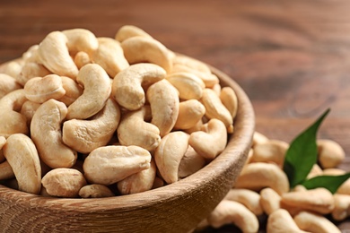 Tasty cashew nuts in bowl on wooden table, closeup