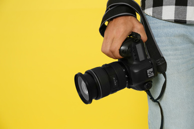 Photo of Professional photographer with modern camera on yellow background in studio, closeup. Space for text