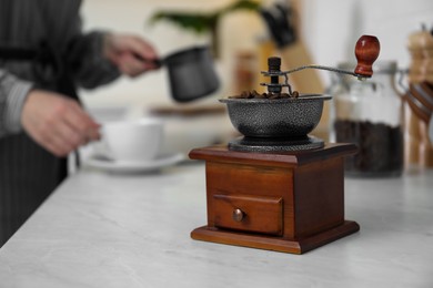 Woman pouring hot drink into cup in kitchen, focus on vintage coffee grinder. Space for text