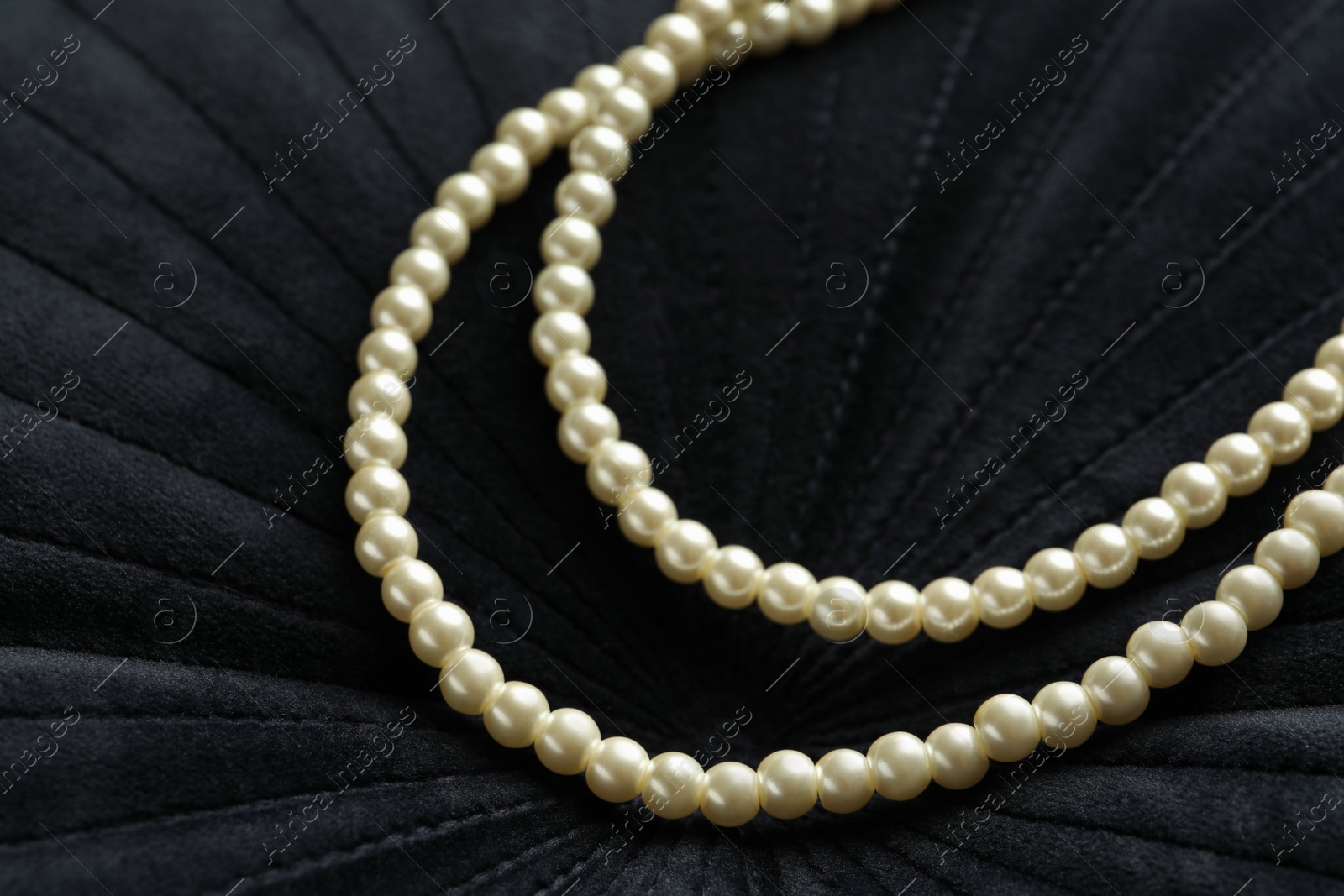 Photo of Elegant necklace with pearls on black fabric, closeup