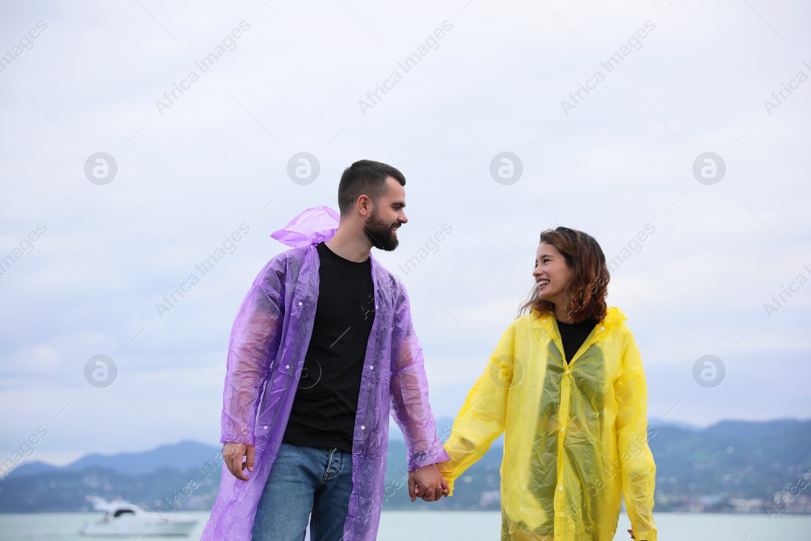 Photo of Young couple in raincoats enjoying time together under rain on beach