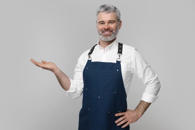 Photo of Happy man wearing kitchen apron on grey background. Mockup for design