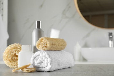 Natural loofah sponges, towel and cosmetic products on table in bathroom. Space for text